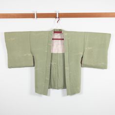 a green kimono hanging on a white wall next to a wooden hanger with a red stripe