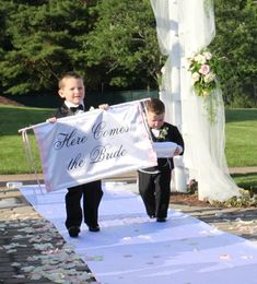 two young boys are walking down the aisle holding a sign that says here comes the bride