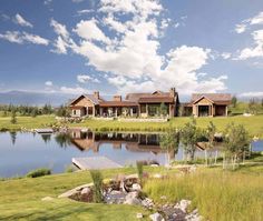 a large house sitting on top of a lush green field next to a lake and forest