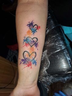 two hearts tattoo on the arm with watercolor paint splatters around it and an ink blotch