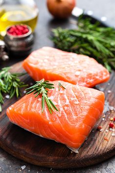 two raw salmons on a cutting board with herbs and seasonings around the edges