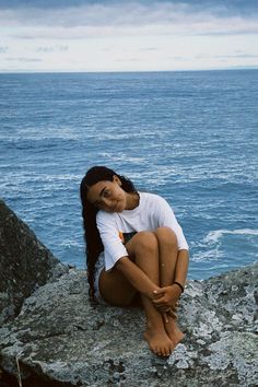 a woman sitting on top of a rock next to the ocean with her head down