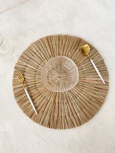 a place setting with two forks, spoons and a glass on a woven table mat