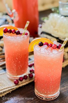 two glasses filled with orange juice and garnished with cranberries on a table