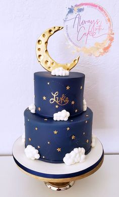 a three tiered blue cake with gold stars and moon on top, sitting on a plate