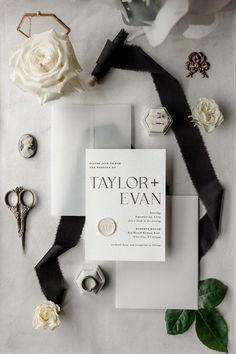 the wedding stationery is laid out with white flowers and black ribbon, brooches