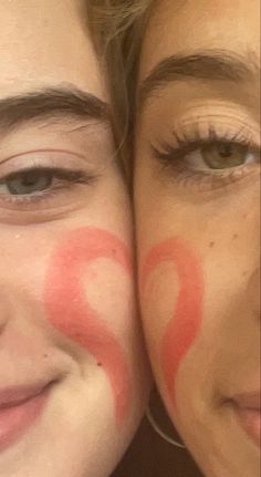 two women with their faces painted red and the words q on them are smiling at the camera