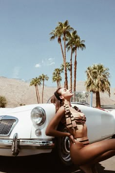 a woman sitting on the hood of a car with palm trees in the back ground