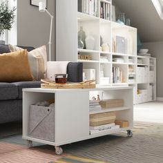 a living room filled with furniture and a book shelf next to a gray couch in front of a window