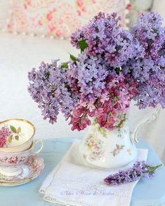 purple flowers are in a vase next to a cup and saucer on a blue table