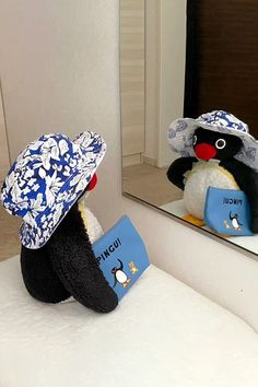 a stuffed penguin with a book in front of a mirror