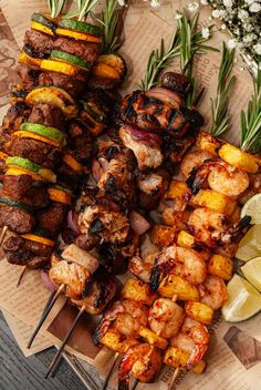 several skewered meats and vegetables are on a wooden platter with lemon wedges