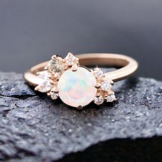 an opal and diamond ring sitting on top of a rock