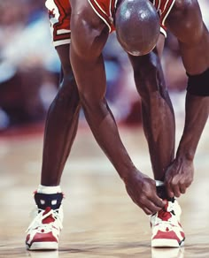 a basketball player tying his shoe on the court with one hand and another leg behind him