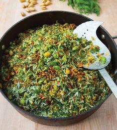 a pan filled with green and yellow food on top of a wooden table next to nuts