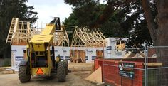 a construction site with a large yellow truck in the foreground and trees on the other side