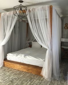 a white bed with sheer curtains on the top and bottom, sitting in a room