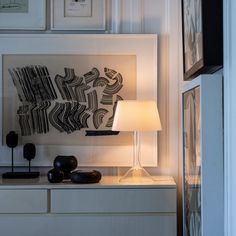 a lamp on a table in front of a wall with pictures and artwork above it