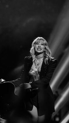 a black and white photo of a woman in a suit holding a guitar on stage