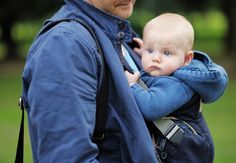 a man holding a baby in his back pack while wearing a blue jacket and backpack