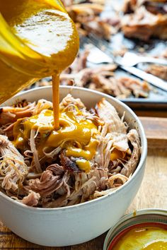 someone pouring mustard into a bowl filled with pulled pork