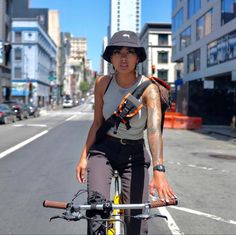 a woman riding a bike down the middle of a city street with tall buildings in the background