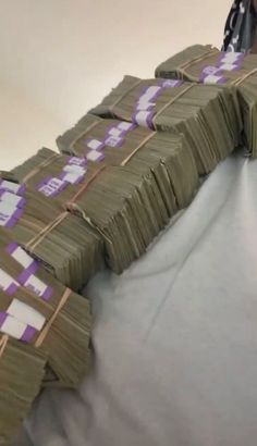 stacks of money sitting on top of a bed covered in white sheets and purple tape