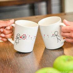 two people holding coffee mugs on top of a wooden table