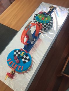 two birthday cakes sitting on top of a plastic wrapper covered table with race track decorations