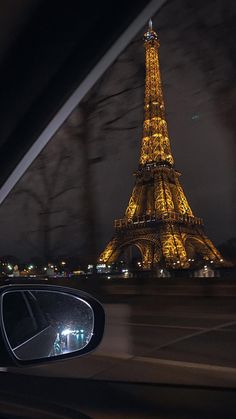 the eiffel tower is lit up at night from behind a car's side view mirror