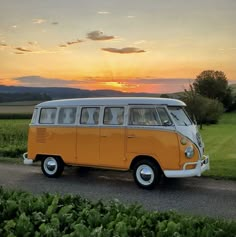 an orange and white vw bus parked on the side of a road at sunset