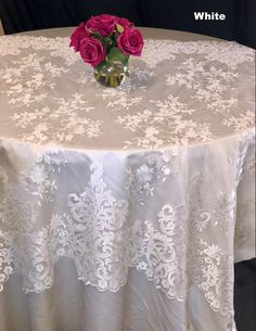 a white table cloth with pink roses in a vase on it and the words white