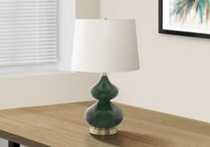 a green lamp sitting on top of a wooden table next to a framed photo and window