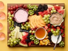 a wooden cutting board topped with fruit and dips