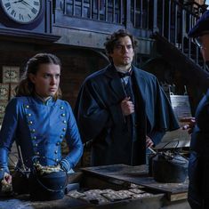 three people standing in front of a table with an old clock on the wall behind them