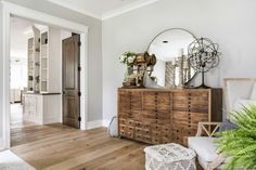 a wooden dresser sitting in the middle of a living room next to a mirror and potted plant