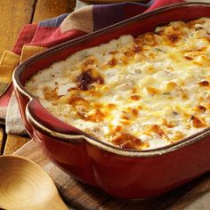 a red casserole dish with cheese and meat in it on a wooden table