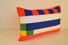 an orange, blue, and green striped pillow on a white table with a light brown wall in the background