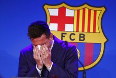 a man in a suit wiping his face at a podium with a barcelona crest behind him