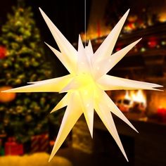 a white star shaped light hanging from a string in front of a christmas tree and fireplace