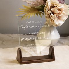 a vase with flowers in it sitting on a white table cloth next to a glass plaque