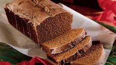 a loaf of chocolate cake sitting on top of a white plate next to a red ribbon