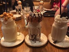 three desserts are sitting on small plates at a table with people in the background