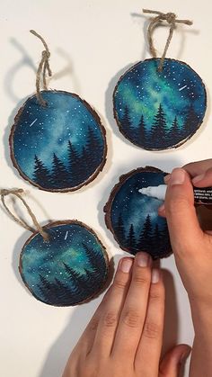 someone is painting three ornaments with blue and green colors on them, while the other hand holds a marker