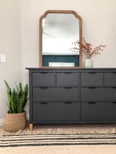 a black dresser with a mirror and potted plant on top in front of it