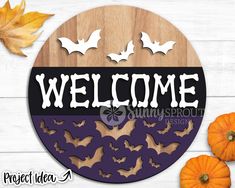 a welcome sign with bats on it next to some pumpkins and leaves in the background