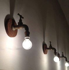 three light bulbs are on the wall next to some pipes and faucet lights