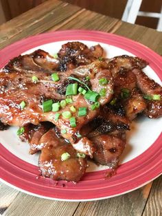 the plate is full of meat with green onions and sauce on it, sitting on a wooden table