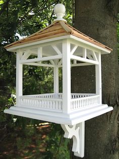 a white bird feeder hanging from the side of a tree