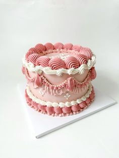 a three layer cake with pink icing and ruffles on the top is sitting on a white surface